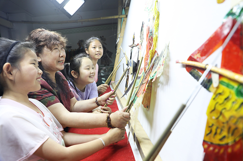 皮影藝人指導小朋友表演皮影戲。