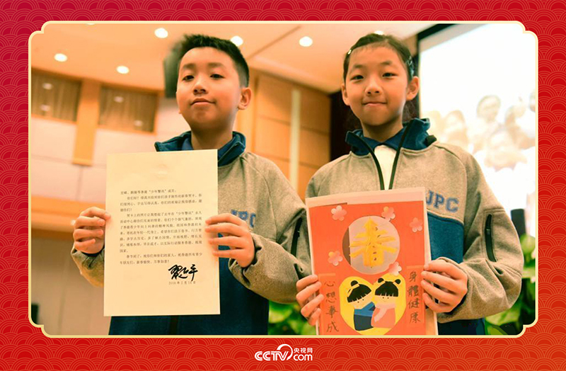 圖為香港“少年警訊”成員郭宏晞（左）展示習(xí)主席回信、羅顥凝（右）展示送給習(xí)主席的賀卡并合影。