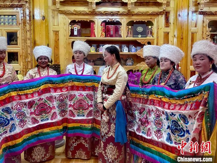 圖為女性展示村民自發(fā)繡制的“百米五彩哈達(dá)”?！±钣穹?攝